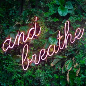 Neon sign reading Just Breathe on a leafy background